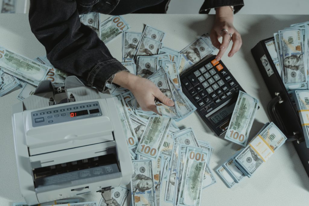 Person Holding Black and Gray Calculator Amid a Pile of Cash